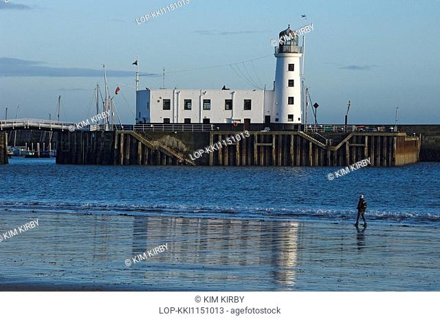 England, North Yorkshire, Scarborough, A lone person walking along the foreshore by Scarborough Lighthouse on Vincent Pier