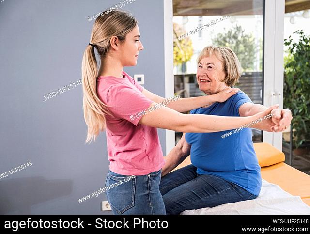 Physiotherapist stretching hand of disabled patient at home