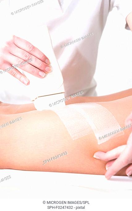 Applying depilation wax on woman's leg in beauty salon