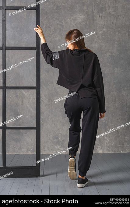 Young woman in black sportswear, pants and sweatshirt. Back view. Concept of fashionable sport outfit, indoors photo
