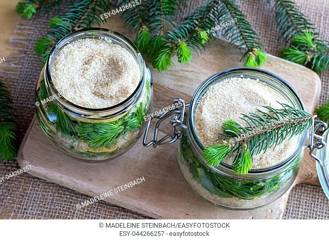 Two jars filled with young spruce tips, lemon and cane sugar, to prepare homemade syrup against cough
