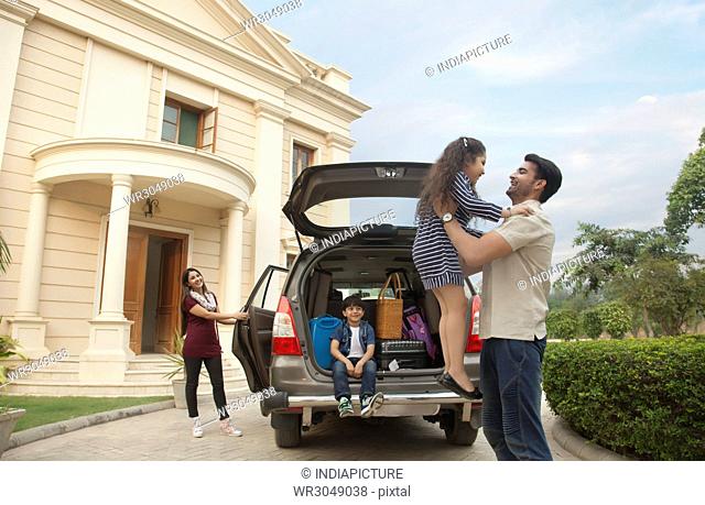 Family standing outdoors by car father lifting daughter