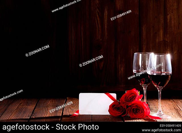 Two glasses of red wine , red roses and blank greeting card on dark wooden background romantic date Valentine day