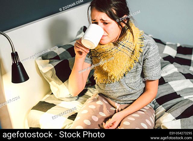 Young beautiful Caucasian woman has a cold, flu with high fever and heat at home in bed. The girl takes headache pills with a glass of water