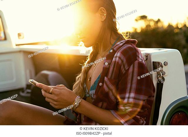 Young woman looking at smartphone from back of pickup truck at Newport Beach, California, USA
