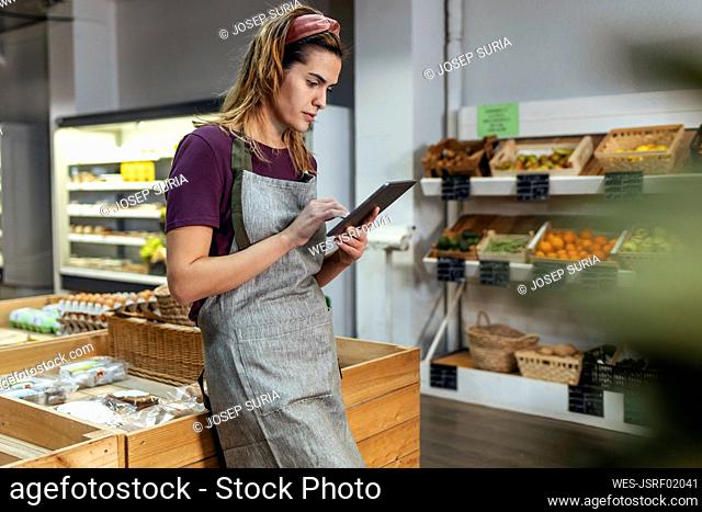 Store owner using tablet PC leaning on crate in organic market