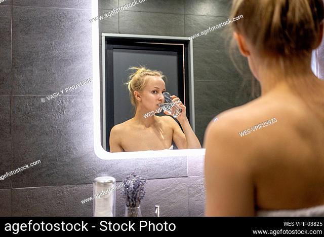 Reflection of woman drinking water in bathroom