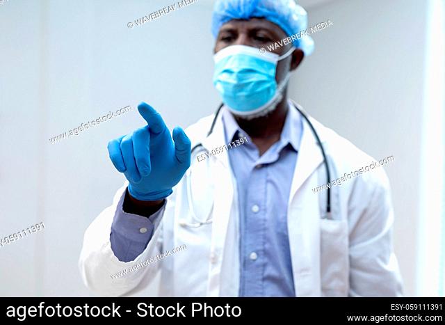 African american male doctor wearing face mask using virtual interactive interface