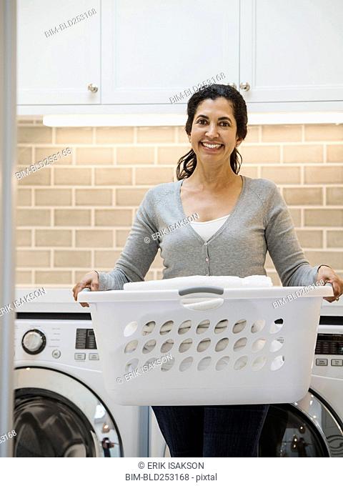 Hispanic woman carrying basket in modern laundry room