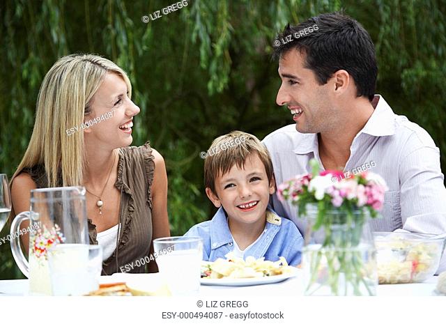 Couple with son 7-9 sitting at table in garden