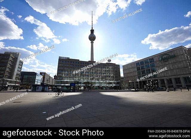 26 April 2020, Berlin: The television tower casts a huge shadow on Alexanderplatz while a person rides his bicycle across the large square