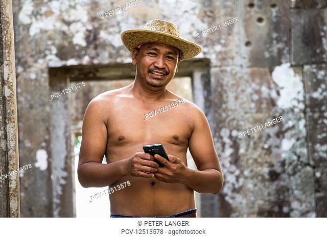 A shirtless Cambodian man holding a smart phone at Preah Vihear; Preah Vihear, Cambodia