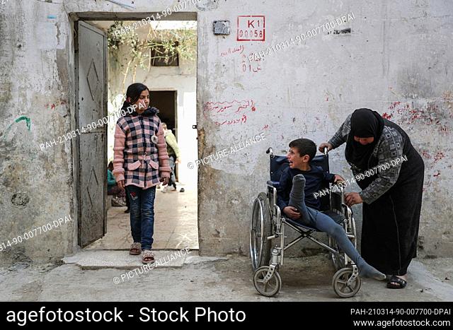 07 March 2021, Syria, Idlib City: A picture made available on 14 March 2021 shows Syrian woman Samiha Seri (R), 63, leaning on the wheelchair of her grandson...