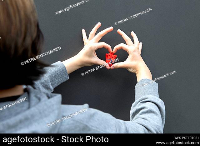 Teenage girl gesturing heart shape on gray background