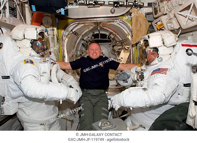 In the Quest airlock, astronaut Barry E. Wilmore (center), STS-129 pilot, assists crewmates Robert L. Satcher Jr. (left) and Mike Foreman, mission specialists