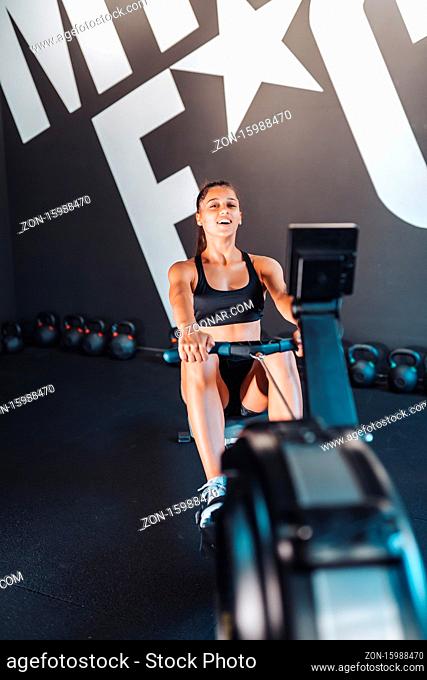 Young woman in sportswear in the gym, training and pulling weights in seated cable row machine