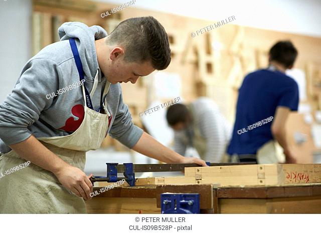 Male teenage carpentry student adjusting wood clamp in college workshop