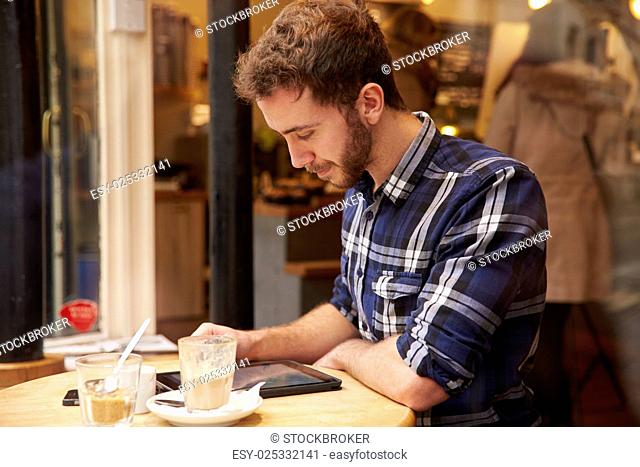 Man Viewed Through Window Of Café Using Digital Tablet