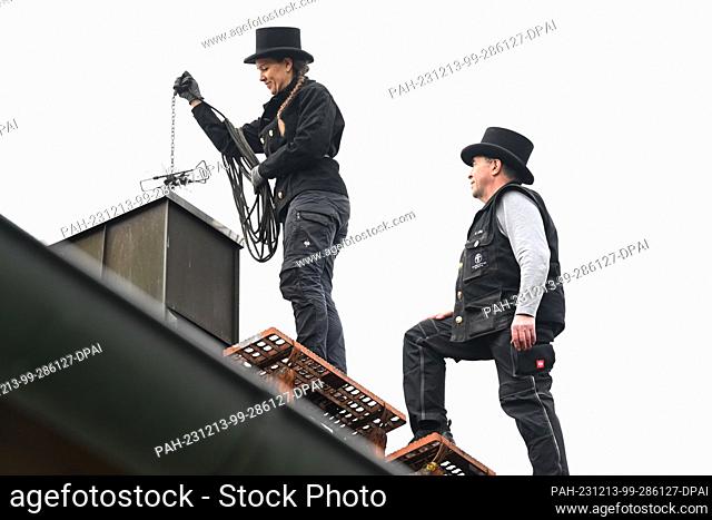 PRODUCTION - 13 December 2023, Bavaria, Munich: Chimney sweeps Udo Löbel (r) and his daughter Diane Loebel stand by a chimney on the roof of a detached house