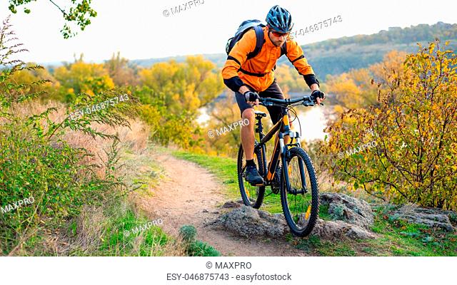 Cyclist in Orange Riding the Mountain Bike on the Autumn Rocky Trail. Extreme Sport and Enduro Biking Concept