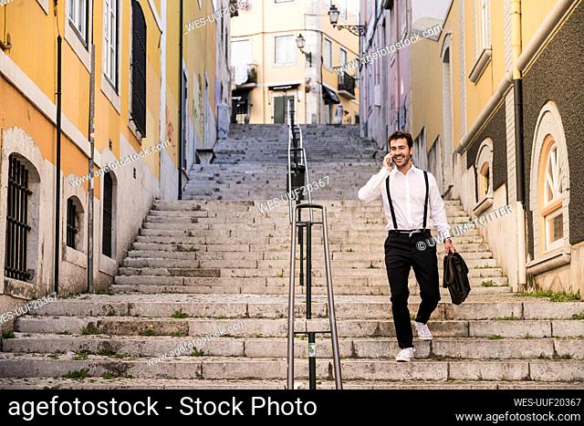 Smiling young man on the phone walking down stairs in the old town, Lisbon, Portugal