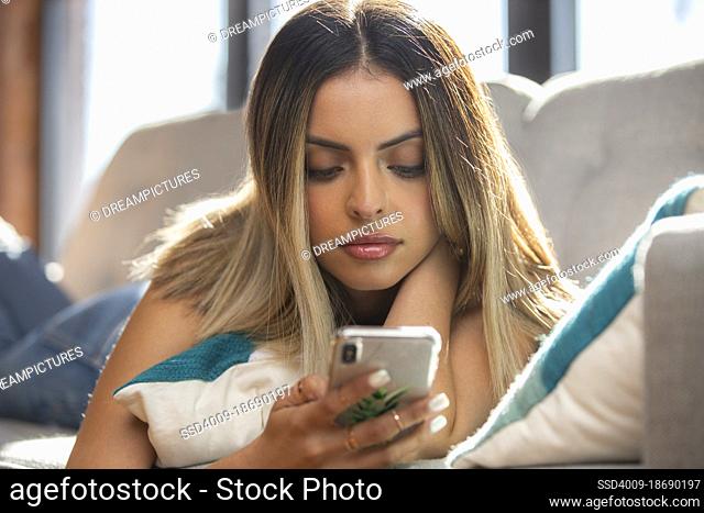 Intimate shot of a happy young woman using mobile phone laying on sofa at home