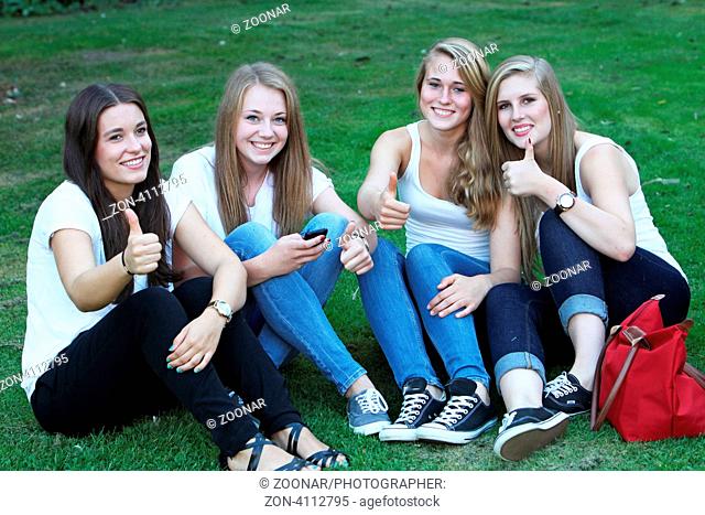 Gruppe junger Mädchen zeigt den Daumen hoch. Sie sitzen im Gras und lächeln
