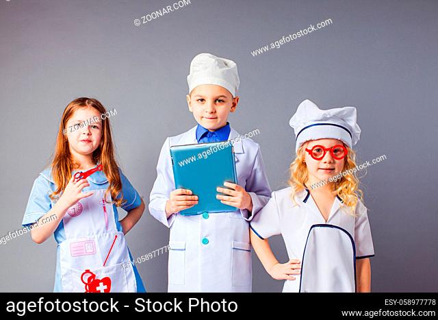 Kids imagine future profession. Cute little doctors on grey background. Children dressed as doctors