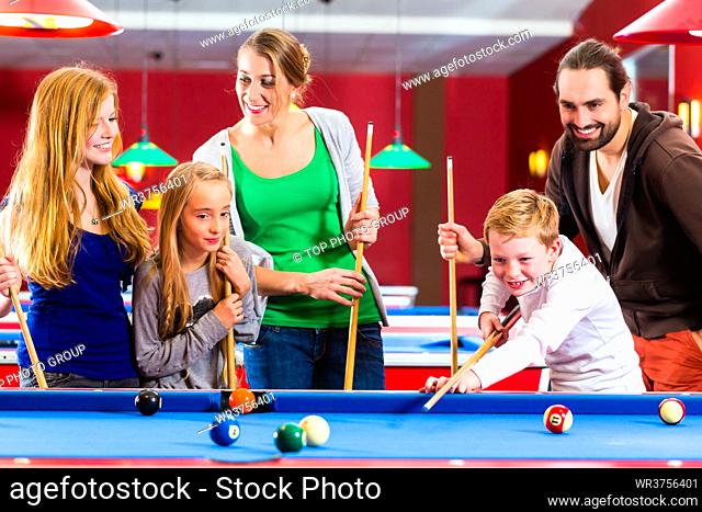Family playing together billiard with queue and balls on pool table