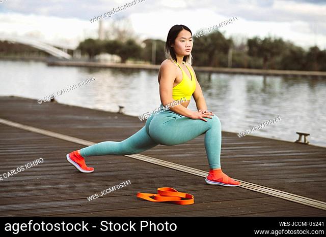 Young athlete doing warm-up exercise on jetty at lakeside