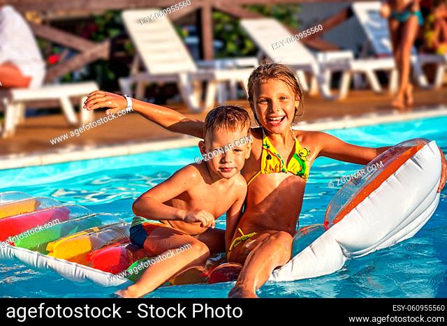 Little children on inflatable mattress in swimming pool. Smiling kids playing and having fun in swimming pool with air mattress