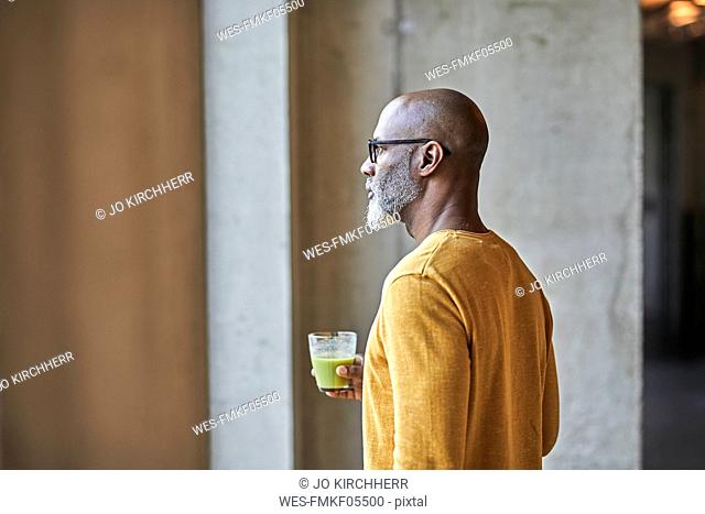 Mature businessman in office holding a smoothie at the window