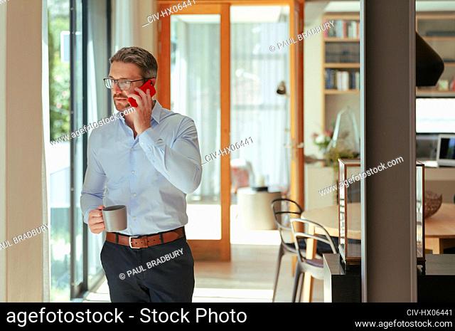 Businessman talking on smart phone and drinking coffee at home