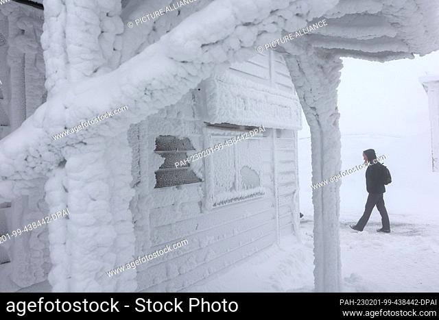 PRODUCTION - 01 February 2023, Saxony-Anhalt, Schierke: A hiker walks along the station restaurant on the Brocken. Strong storms with snow and freezing rain...