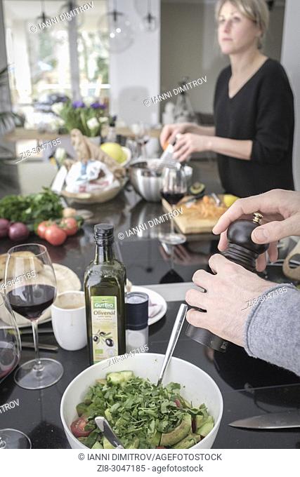 Preparing vegetarian meal together - seasoning green salad, contemporary kitchen setting