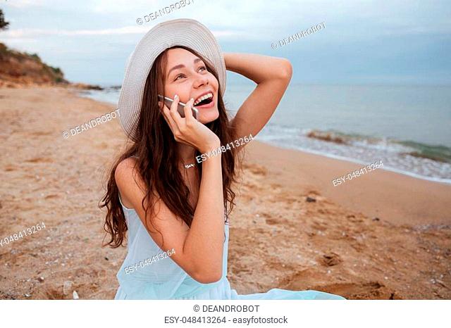 Happy pretty young woman talking on mobile phone and laughing on the beach