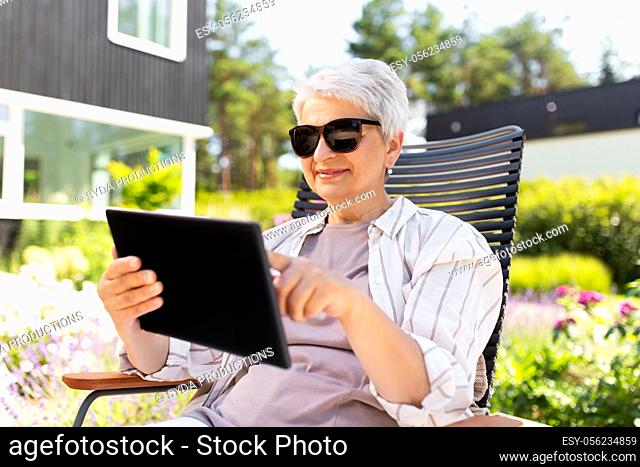 happy senior woman with tablet pc at summer garden
