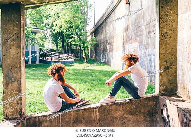 Young male hipster twins with red beards sitting on wall