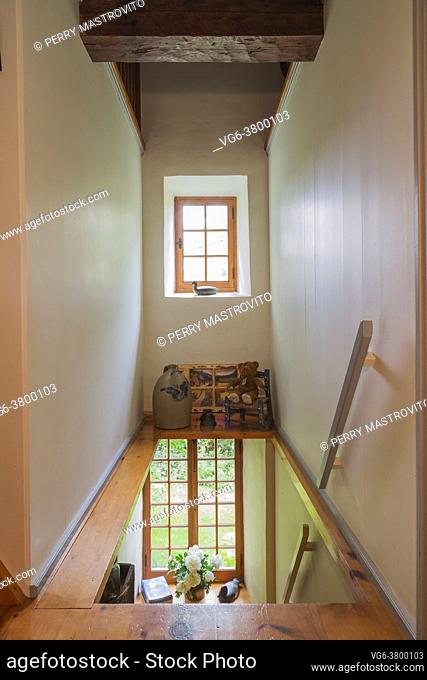 Small mezzanine decorated with ceramic jug, teddy bear on a chair and painted landscaped scenes on repurposed window panes above pine wood staircase and...