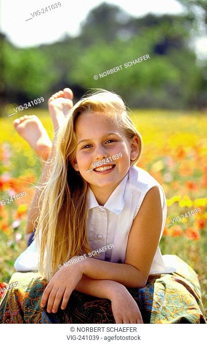 portrait, smiling girl, with long blond hair, 12 years, white sleeveless blouse, sits on a meadow sprinkeled with corn poppies and yellow flowers  - GERMANY