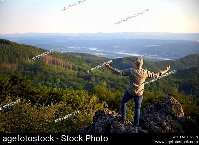 Male hiker standing with arms outstretched on top of mountain at sunset