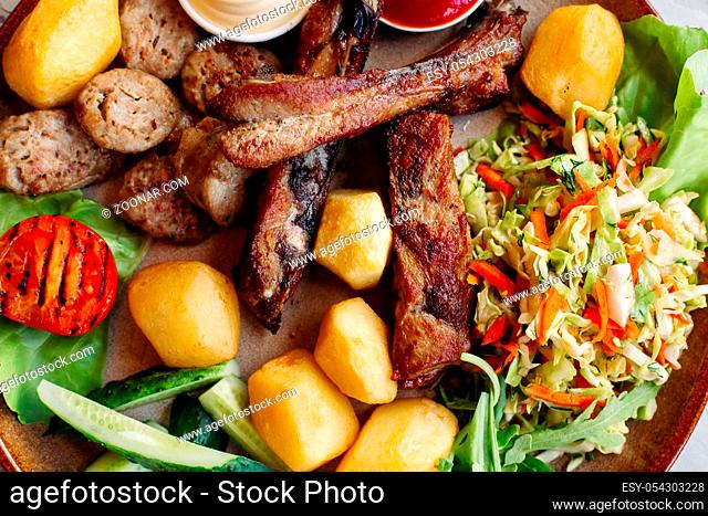 Colorful top view of tasty restaurant meal. clay plate including sausages, cucmbers, boiled potatoes, grilled chicken legs, roasted onion