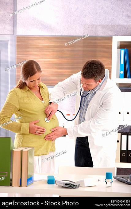 Woman at doctor's office at pregnancy consultation, doctor examining with stethoscope