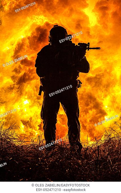 Backlit silhouette of special forces marine operator in forest on fire explosion background. Battle, bombs exploding, fighting no matter what