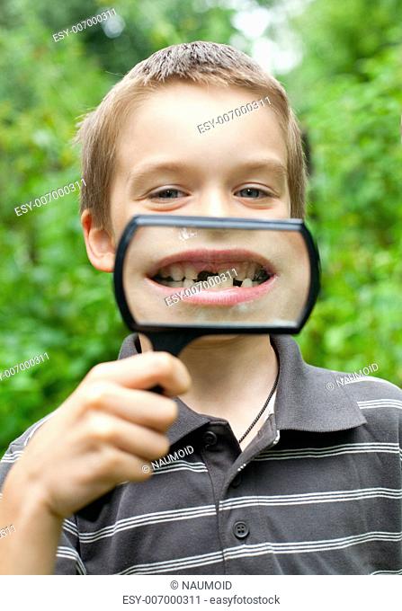 Young boy showing missing baby tooth through hand magnifier, shallow DOF