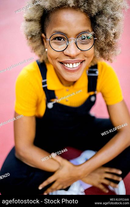 Smiling woman with eyeglasses sitting on footpath