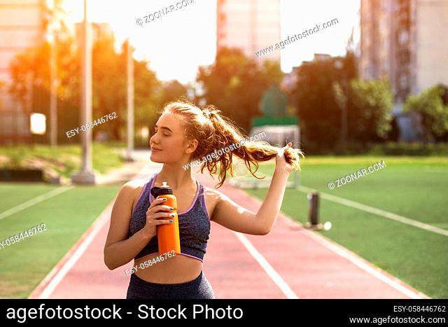 Beautiful Female Sportsman is Posing for Camera. Young Girl Closes Eyes and Touches Ponytail Dreamingly. Future Winner is on Training