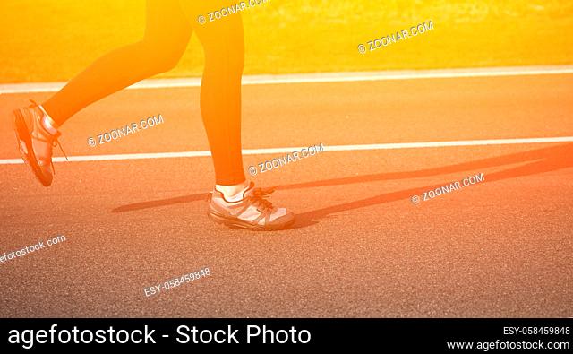 Shallow depth of field, toned with instagram like filter, flare effect. Closeup of female in running shoes going for run on road at sunrise or sunset