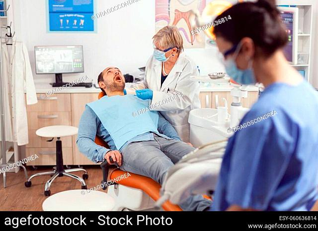 Sick patient sitting on dental chair with open mouth while senior dentist woman analyzing health teeth before medical surgery