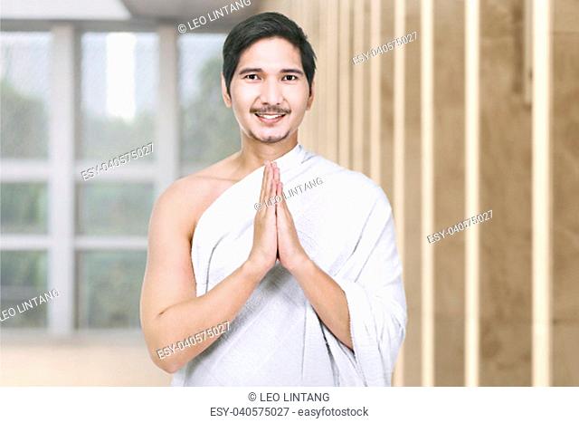 Happy asian hajj pilgrim with hand gesture praying on the mosque